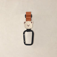 つぶらな瞳が可愛いクマのモチーフをあしらった、ブラウンのペットカートフック単体写真。マットな質感のパーツと光沢のあるカラビナの対比。