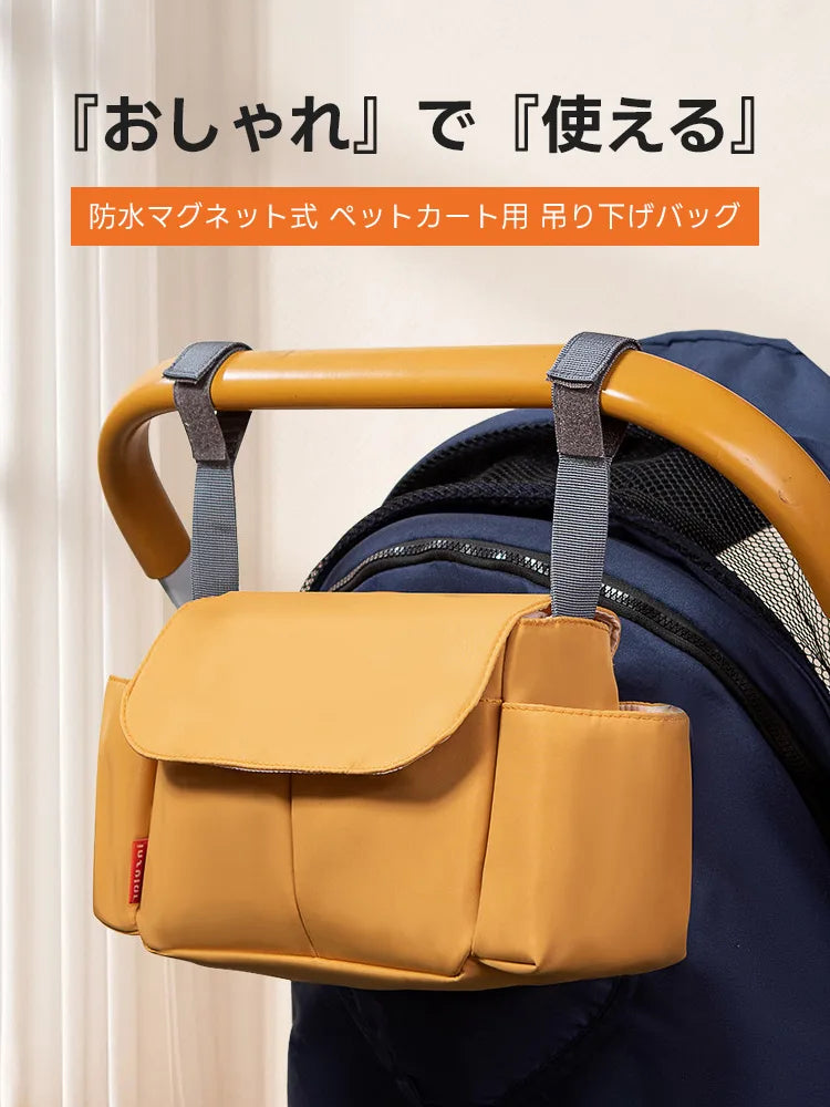 マスタードイエローカラーの2WAY防水カートバッグをペットカートのハンドルに吊り下げた状態。グレーの太めのストラップでしっかりと固定され、フラップ部分のマグネットやサイドのボトルポケットが確認できます。