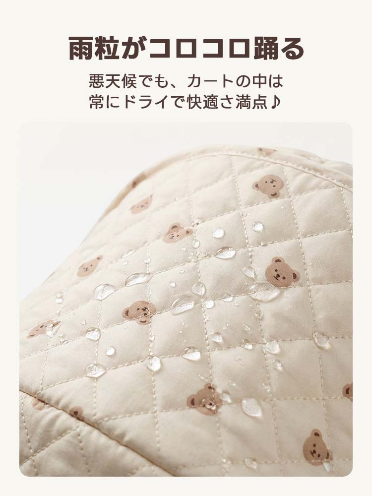 ミルク ベージュのくま柄キルティングの上で、雨粒が玉のように弾かれている接写。急な雨や雪でも生地に染み込ませず、カート内部を常にドライに保つ高い撥水性能を視覚化。