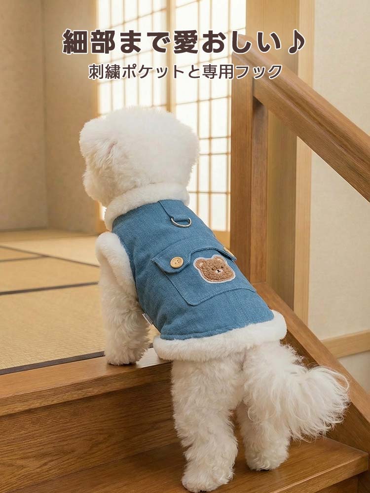 木目調の床に立つ白い小型犬が、もこもこの裏ボアがついたブルーのデニムベストを着用。厚手ながらもスリムなシルエットで、着ぶくれせずに自由に動けるデザイン。背中のクマ刺繍とボタン付きポケットが目を引く。