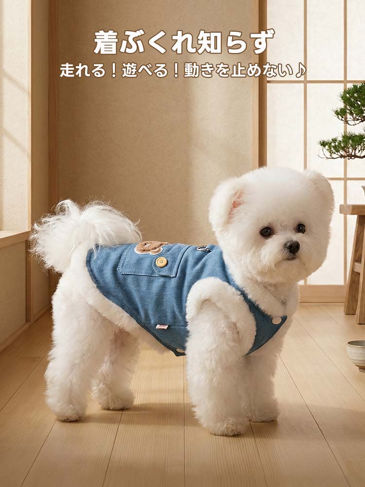 木目調の床に立つ白い小型犬が、もこもこの裏ボアがついたブルーのデニムベストを着用。厚手ながらもスリムなシルエットで、着ぶくれせずに自由に動けるデザイン。背中のクマ刺繍とボタン付きポケットが目を引く。