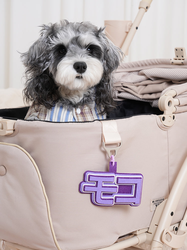 ベージュのペットカートに装着された「モコ」のフェルトチャーム。紫色のグラデーションがシックで、もこもこした立体的な文字が視線を集めます。名入れによる特別なカスタムで、いつものカートが世界にひとつの「特別な場所」に変わります。