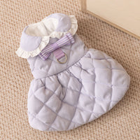  淡いラベンダーカラーの犬用キルティングワンピース。白いフリル襟とストライプ柄のリボンが特徴で、背中には頑丈な金属製Dカンが配置されています。ふっくらとした格子模様のキルト生地が上品な質感の一着です。