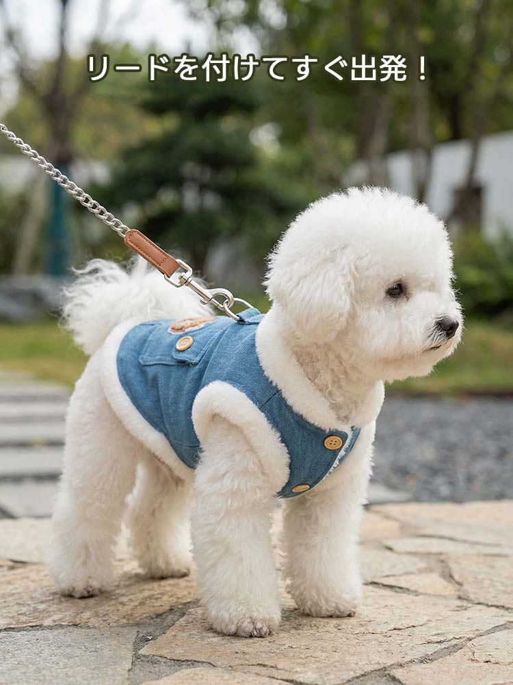 石畳を歩く白い小型犬が、背面のリングにリードを装着した状態。裏ボアの白い縁取りが際立つデニムベストは、ハーネス不要でそのまま外出可能。クマの刺繍ポケットが可愛らしく、機能的なフックが安全な歩行を支援。